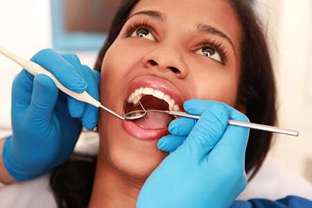The image shows a person receiving dental treatment, with a dental hygienist performing a cleaning procedure while wearing blue gloves and using dental tools, including a mirror and brush.