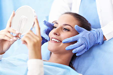 The image shows a woman lying on a medical table with a mirror above her face, while a healthcare professional stands beside her holding up a magnifying glass, seemingly inspecting her skin or facial area.