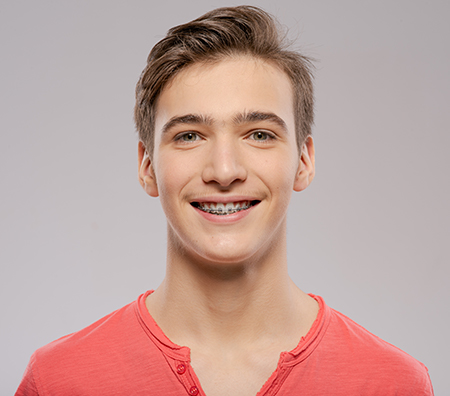 The image shows a young man with a smile, looking directly at the camera, against a plain background.